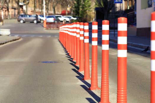 Red reflective road columns divide the road in half amid the entrance to the parking in a blur in the sunlight.