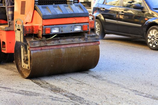 Heavy vibrating rink rides along the road on asphalt pavement on a city street.