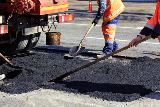 The road workers' working group renews a part of the road with fresh asphalt and levels it for repair in road construction.