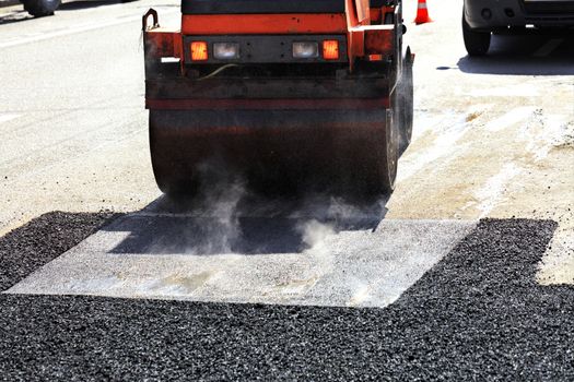 Heavy vibrating roller repairs the road on the repaired asphalt surface on a clear sunny day