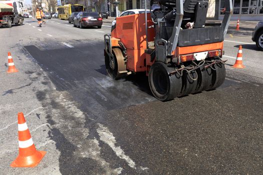 A heavy vibratory skating rink is repairing a section of the road fenced off by traffic cones on a city street.