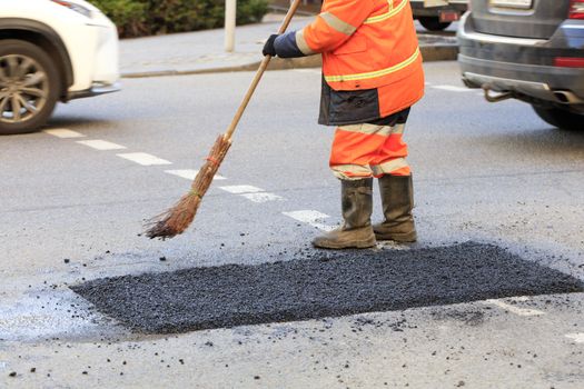 The road worker sweeps with a panicle away with fresh asphalt on the repaired stretch of road in road construction.
