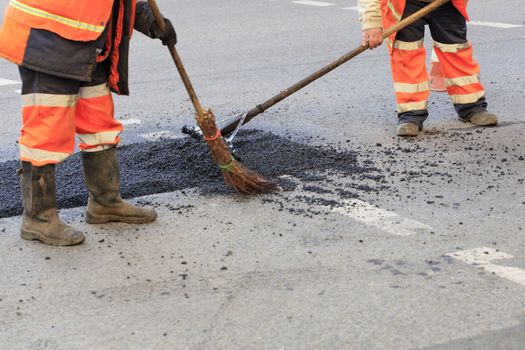 Two road builders with a whisk and level sweep and level fresh asphalt on the repaired stretch of road in road construction.