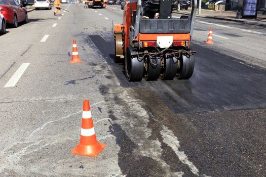 Road red cones enclose a section of the road on a city street for repairing asphalt pavement and work of road roller