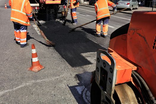 The working team renews a part of the road with fresh asphalt and prepares a section for rolling with a road roller.