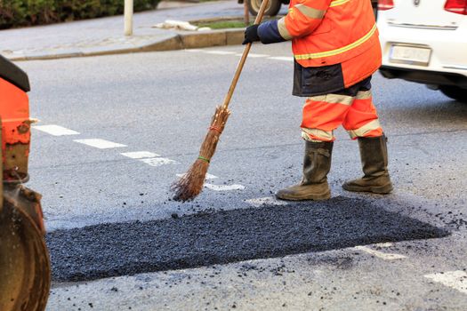A road worker levels a fresh asphalt by a wooden level on a repaired road section in road construction.