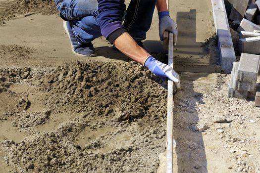 The worker aligns the foundation on a wooden level and prepares a platform for the final laying of paving slabs.