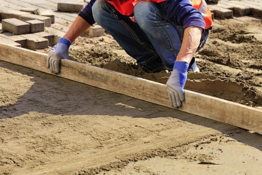 The worker aligns the foundation with a wooden level to continue paving paving.