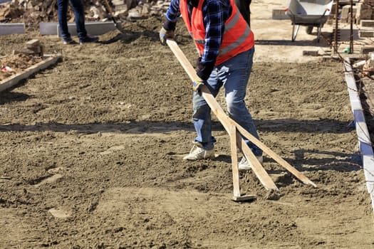 The worker aligns the foundation with a wooden level to begin laying paving slabs on the working area.