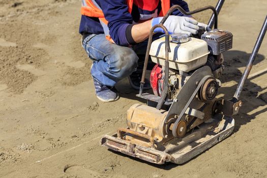 Old worn gasoline compactor regularly needs cleaning for further work on the compaction of sandy soil.