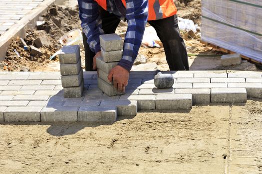 Worker brings a stack of paving slabs to lay it on the prepared flat sandy ground on the sidewalk.