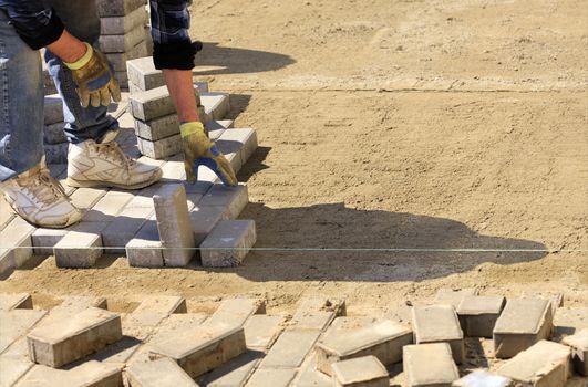 The worker puts the paving slabs along the stretched thread on the prepared flat sandy ground on the sidewalk.