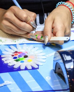 A master manicure artist draws a floral design of beautiful female nails with a red rose manicure on light green.