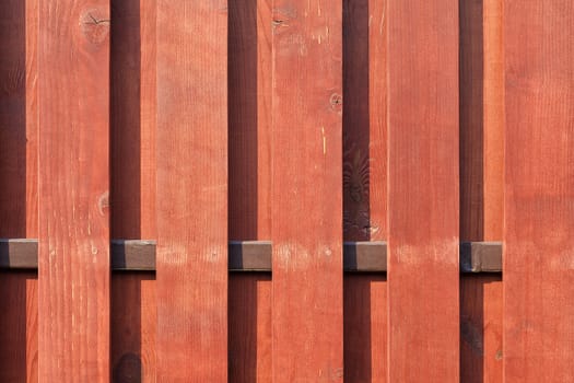 A new vertical wooden fence with a transverse brown plank, painted with protective red-brown impregnation.