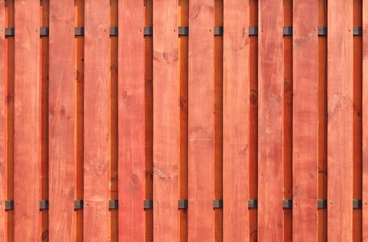 A new vertical wooden fence with two transverse brown guides, painted with protective red-brown impregnation.