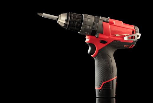 Cordless drill driver in red with rubberized handle in profile, isolated on black background with reflection