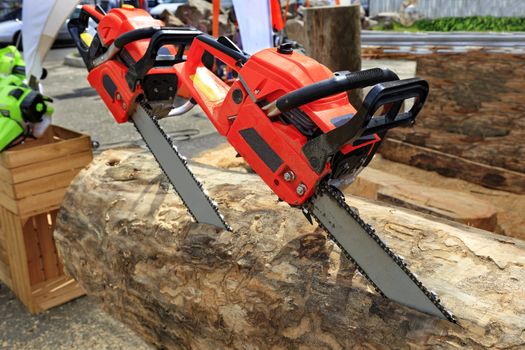 Red powerful chainsaws protrude from the log. The concept of cutting wood.