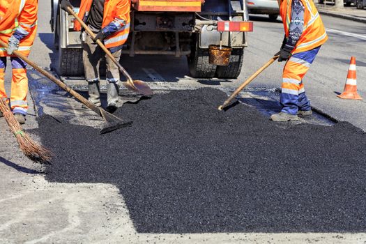 The road workers' working group updates part of the road with fresh hot asphalt and smoothes it for repair.