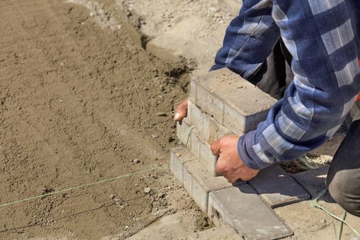 Worker pulls the nylon cord over the prepared flat sandy soil for laying paving slabs.