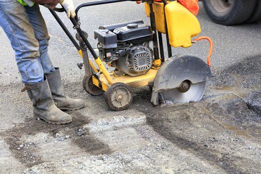 The road technician starts the engine of a gasoline diamond saw to remove old asphalt during repairs on the roadway.