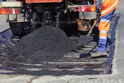 The road service worker shovel new asphalt during construction and patching of the road.