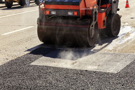 Heavy vibrating roller compacts hot asphalt on the repaired asphalt surface of the carriageway on a clear sunny day
