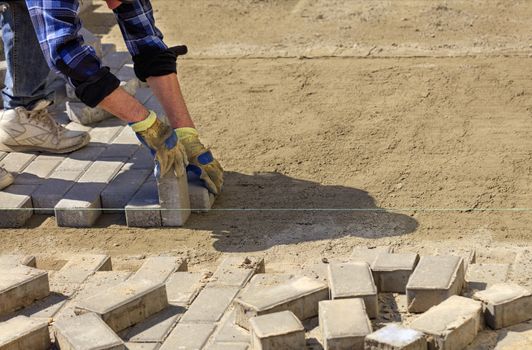 The worker lays the pavement along the tensioned cord on the prepared flat sandy soil on the sidewalk.