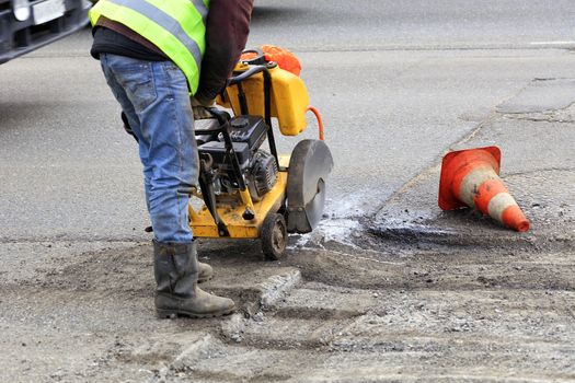 An employee of the road maintenance service removes old asphalt with a gasoline carver during repairs on the carriageway.