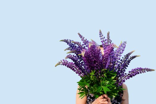 A large bouquet of flowers is held in the hands of a girl. Purple lupines on a blue background. Banner space for text. Gift, Holiday, Florist, Discount, Flower Shop