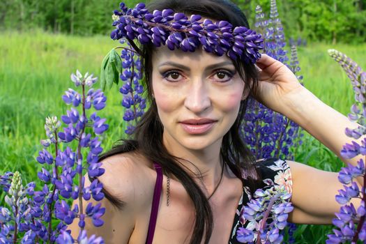 A beautiful woman with a flower wreath on her head rests on a blooming field of lupines on a Sunny summer day