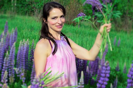 A beautiful woman with a flower wreath on her head rests on a blooming field of lupines on a Sunny summer day