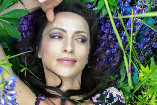 A beautiful woman is relaxing in nature among blooming purple lupines on a Sunny summer day