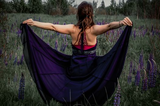 A beautiful woman with a flower wreath on her head rests on a blooming field of lupines on a Sunny summer day. Tinted photo