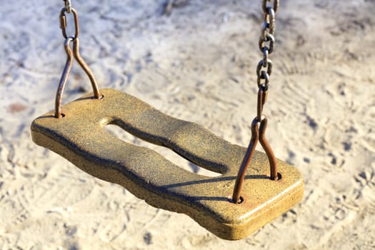 The seat of the old children's swing on a metal chain against the background of worn light sand
