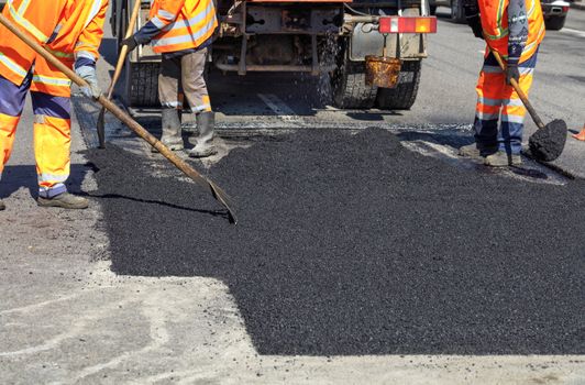 The road workers' working group updates part of the road with fresh hot asphalt and smoothes it for repair.