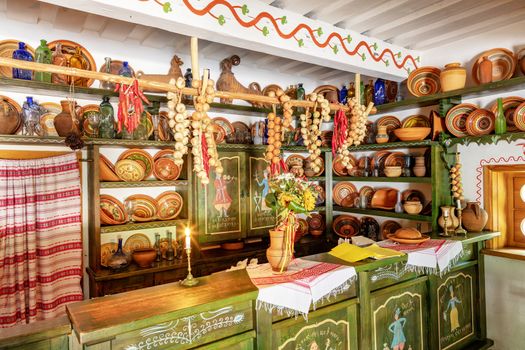 Ceramic painted bowls, plates and jugs on a wooden shelf on the wall, an old counter with glassware in the interior of an old Ukrainian rural cafe and shop.