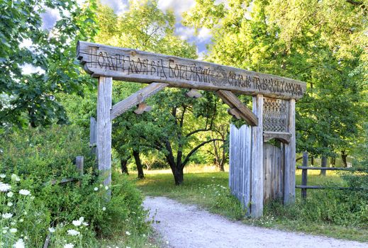 Old Ukrainian wooden gates on the territory of the Cossack settlement on a hill in the middle of the woods with the inscription wise words My help from God, who saves the righteous in the heart.