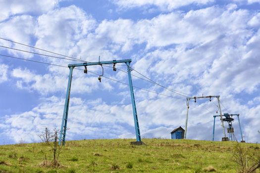 The frame of the mountain cable lift stands apart on the top of the mountain against the background of a deep blue sky with white clouds in the Carpathians.