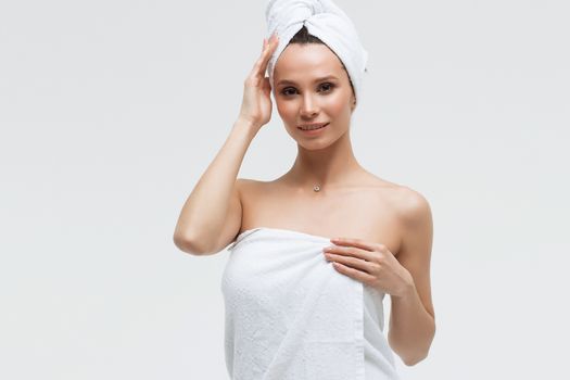 Sensual woman in fluffy white towel on head looking at finger touching towel on body