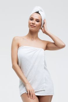 Sensual woman in fluffy white towel on head looking at finger touching towel on body