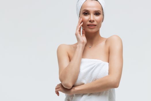 Sensual woman in fluffy white towel on head looking at finger touching towel on body