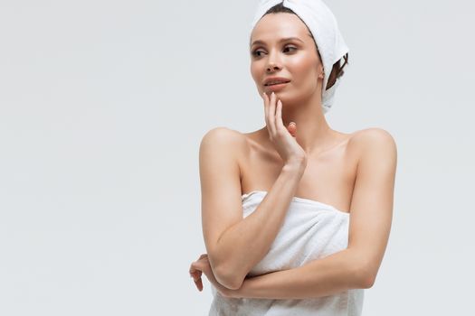 Sensual woman in fluffy white towel on head looking at finger touching towel on body