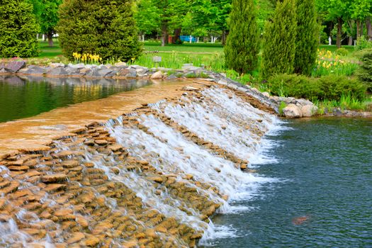A beautiful decorative waterfall refreshes the space in hot weather in a summer city park.