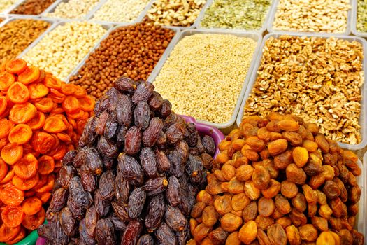Slides with dates close-up, dried apricots, prunes against the background of various nuts in a blurred are sold form on the shelves of the eastern market.