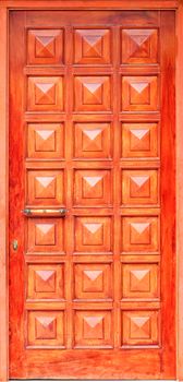 Old wooden entrance doors with a metal bronze handle, framed on the facade with square panels from top to bottom.