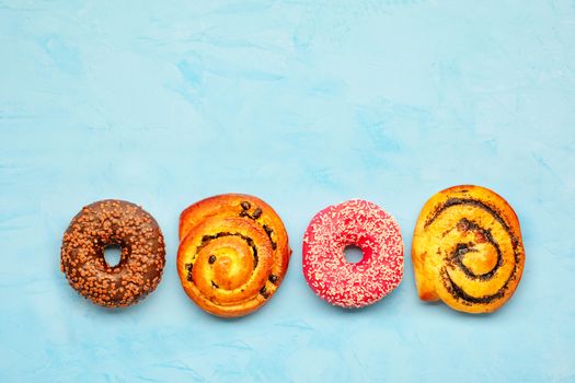 Delicious donuts with chocolate and strawberry icing and buns with poppy seeds and freshly baked raisins, close-up on a light turquoise surface. Pastry sweets for breakfast, image with copy space.