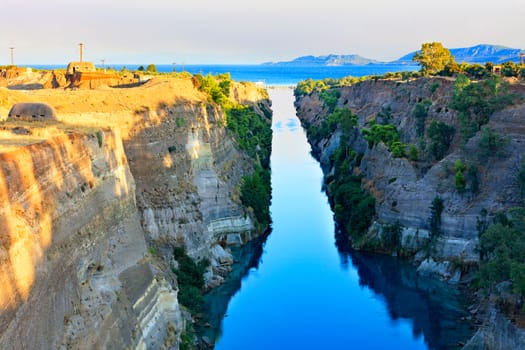 The Corinth Canal in the morning summer day illuminates the bright rising sun of Greece, a view of the Gulf of Corinth from the height, the channel connects the Saronicos of the Aegean Sea and the Corinthian Gulf of the Ionian Sea.