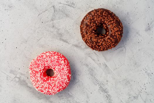 Two delicious donuts with chocolate and strawberry icing sprinkled with coconut and fruit chips on top, close-up on a gray concrete surface. Pastry sweets for breakfast, image with copy space.