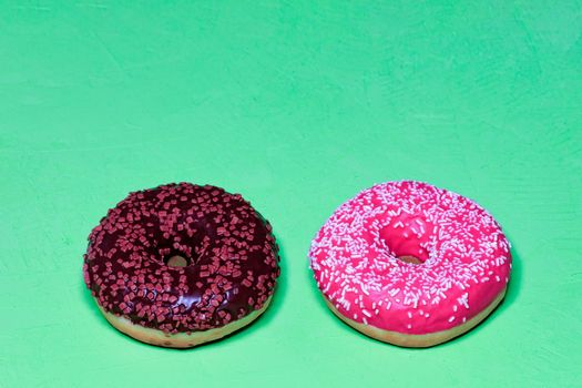 Two delicious donuts with chocolate and strawberry icing sprinkled with coconut and fruit chips on top, close-up on a light green rough surface. Pastry sweets for breakfast, image with copy space.