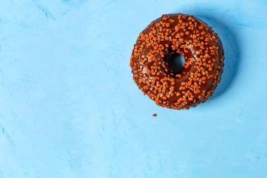 Delicious donut with chocolate icing sprinkled with fruit chips on top, close-up on a blue concrete surface. Pastry sweets for breakfast, image with copy space.